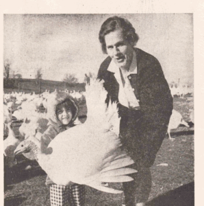A woman and a young girl standing cheerfully, holding a turkey at Wilson Turkey Farm.