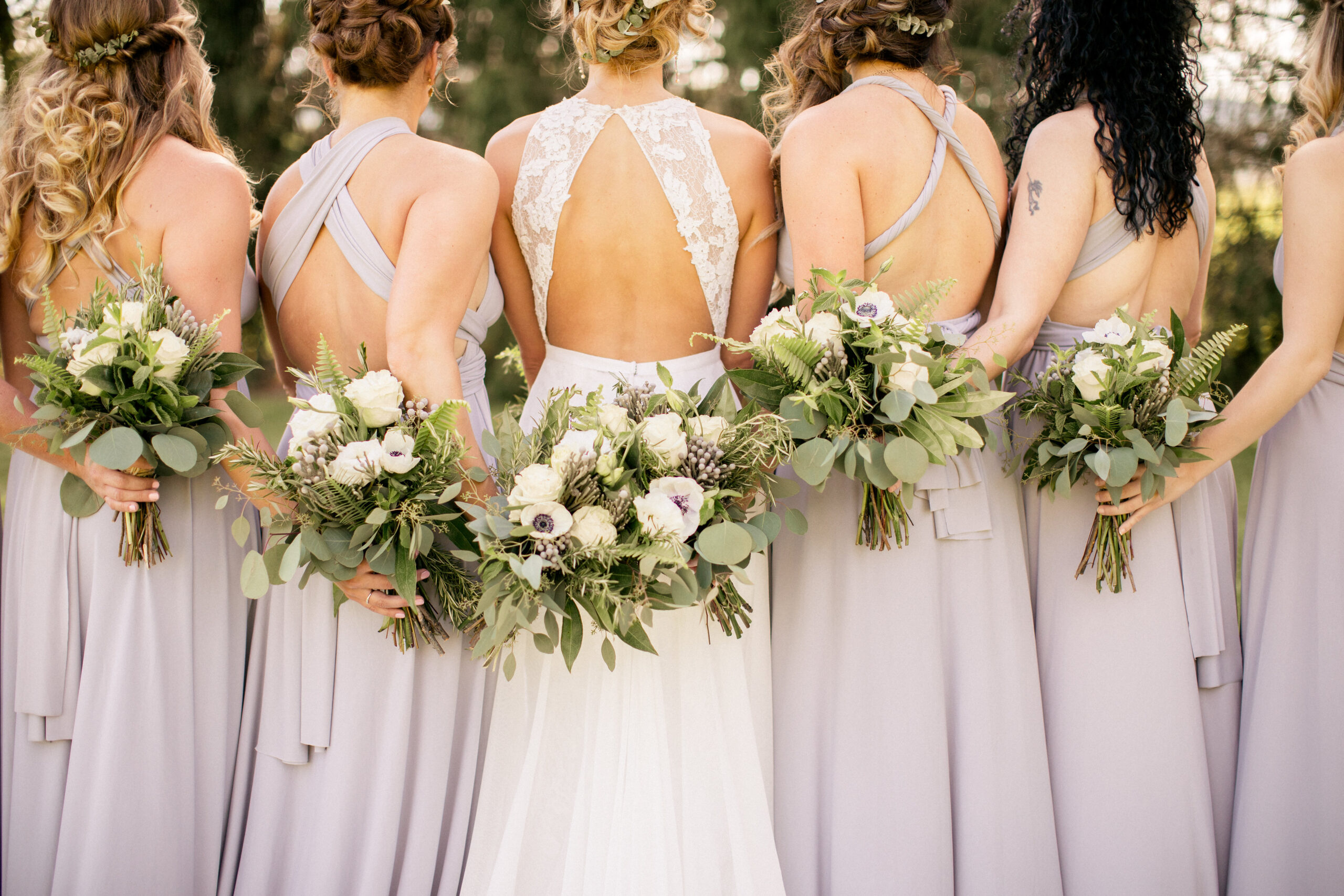 Bridesmaids link arms around each other's backs, holding their floral bouquets.